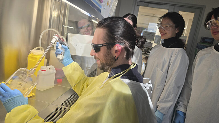 Dr. Christopher Denes works with PROTEUS in the laboratory, conducting molecular evolution experiments while colleagues observe the groundbreaking biological artificial intelligence system in action. Image credit: Dr. Christopher Denes