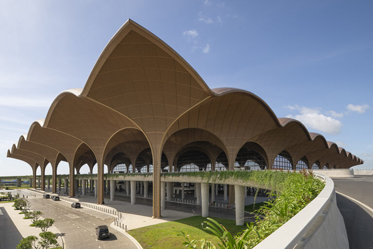 Steel columns expand into a vaulted roof at the Techo International Airport. The structural "trees" branch upward to support the modular canopy, which extends beyond the terminal to shade arrival areas and reduce heat gain in the tropical climate