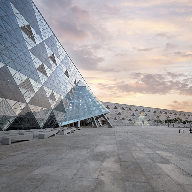 Glass pyramid entrance set against a pastel sunset in front of the museum façade.