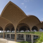 Steel columns expand into a vaulted roof at the Techo International Airport. The structural "trees" branch upward to support the modular canopy, which extends beyond the terminal to shade arrival areas and reduce heat gain in the tropical climate. Photography by Nigel Young.