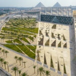 Aerial panorama of the Grand Egyptian Museum and pyramids with patterned palm gardens and stone plazas.