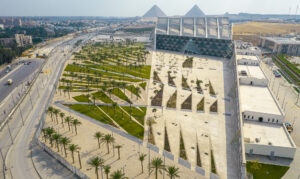 Aerial panorama of the Grand Egyptian Museum and pyramids with patterned palm gardens and stone plazas.