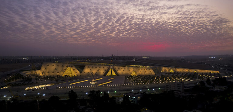 Long night panorama of the museum lit in gold beneath a violet sky.
