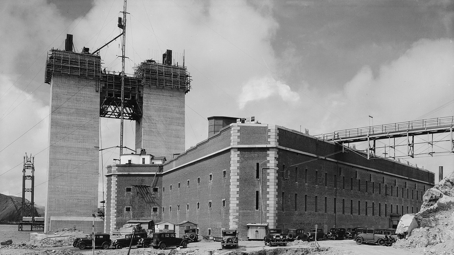 Fort Point’s brick walls in San Francisco, with the concrete south tower of the Golden Gate Bridge under construction behind it, 1934
